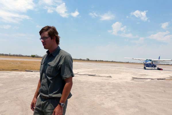 A man standing in front with the small plane in the back, parked on the runway.